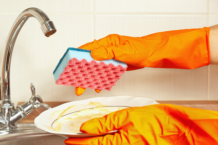 Hands in rubber gloves with dirty dishes over the sink in kitchen